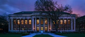 A photo of Walter Library just after sunset. The windows show warm golden light from within, while the sky behind the building is darkening with blue, purple, and pink hues.