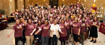 Libraries staff gather in the Great Hall of Walter Library to celebrate its 100 years. They're posed together wearing matching maroon t-shirts for the event.