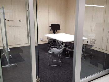 Glass-walled study room with table, chairs, monitor, and whiteboard