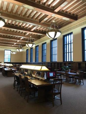 Space with high ceiling with wood beams. Long study tables and chairs. 