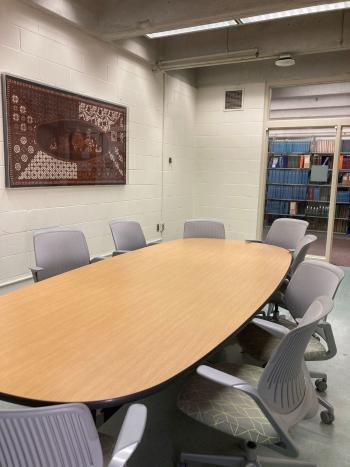 Conference table with 7 chairs, glass rear wall, and hanging art.