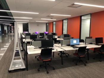 Large open-plan room with tables, computers, chairs and moveable white boards