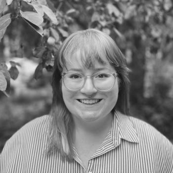 Picture of the librarian, Stephanie Sparrow, featuring a person with long hair and glasses smiling in front of a tree