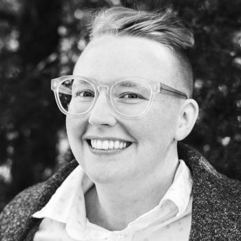 Headshot of Emerson, a White, early 30s person with short hair, clear rimmed glasses, and a light collared shirt. They are looking at the camera and smiling.